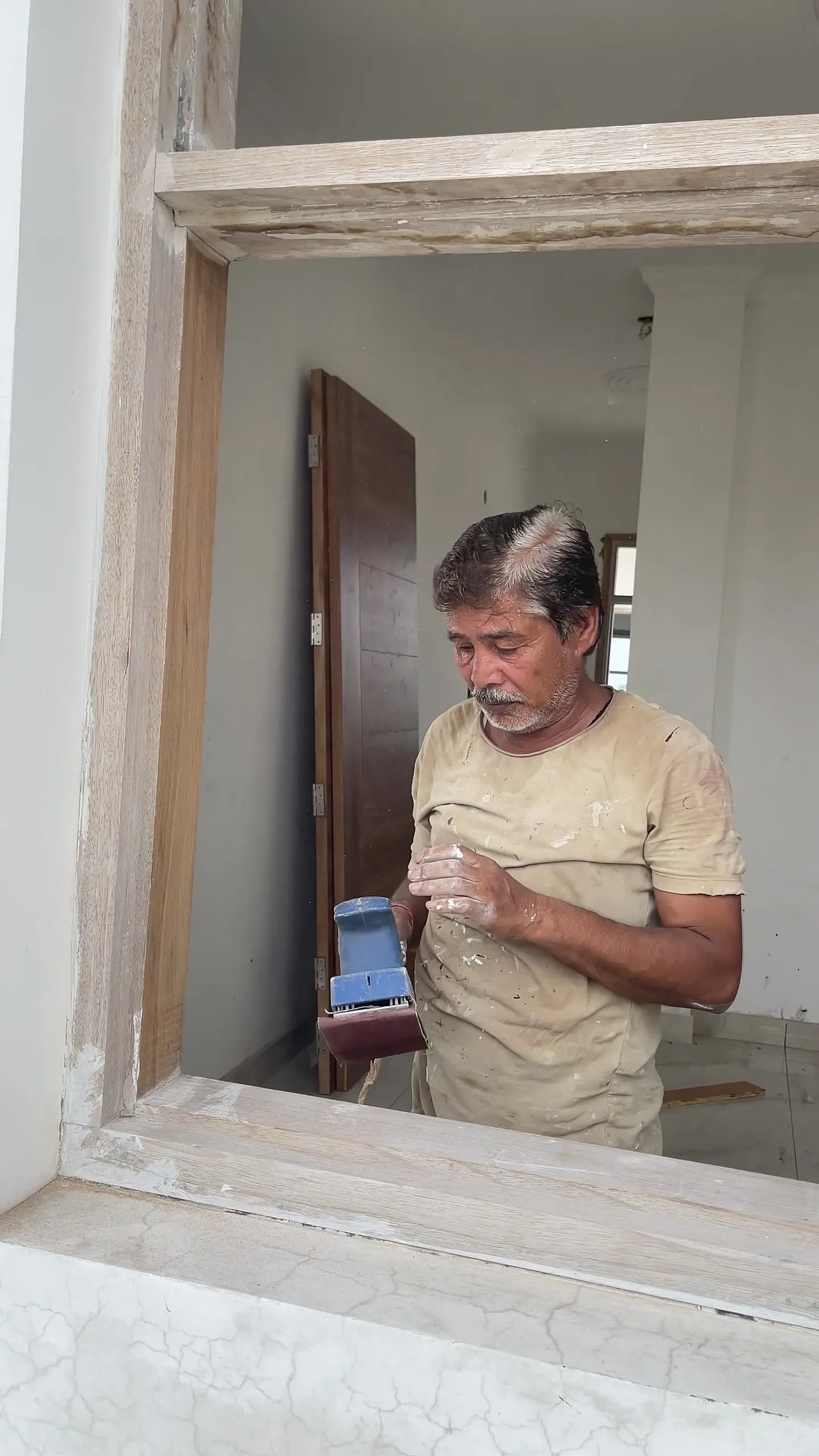 Craftsman sanding a window frame inside a home