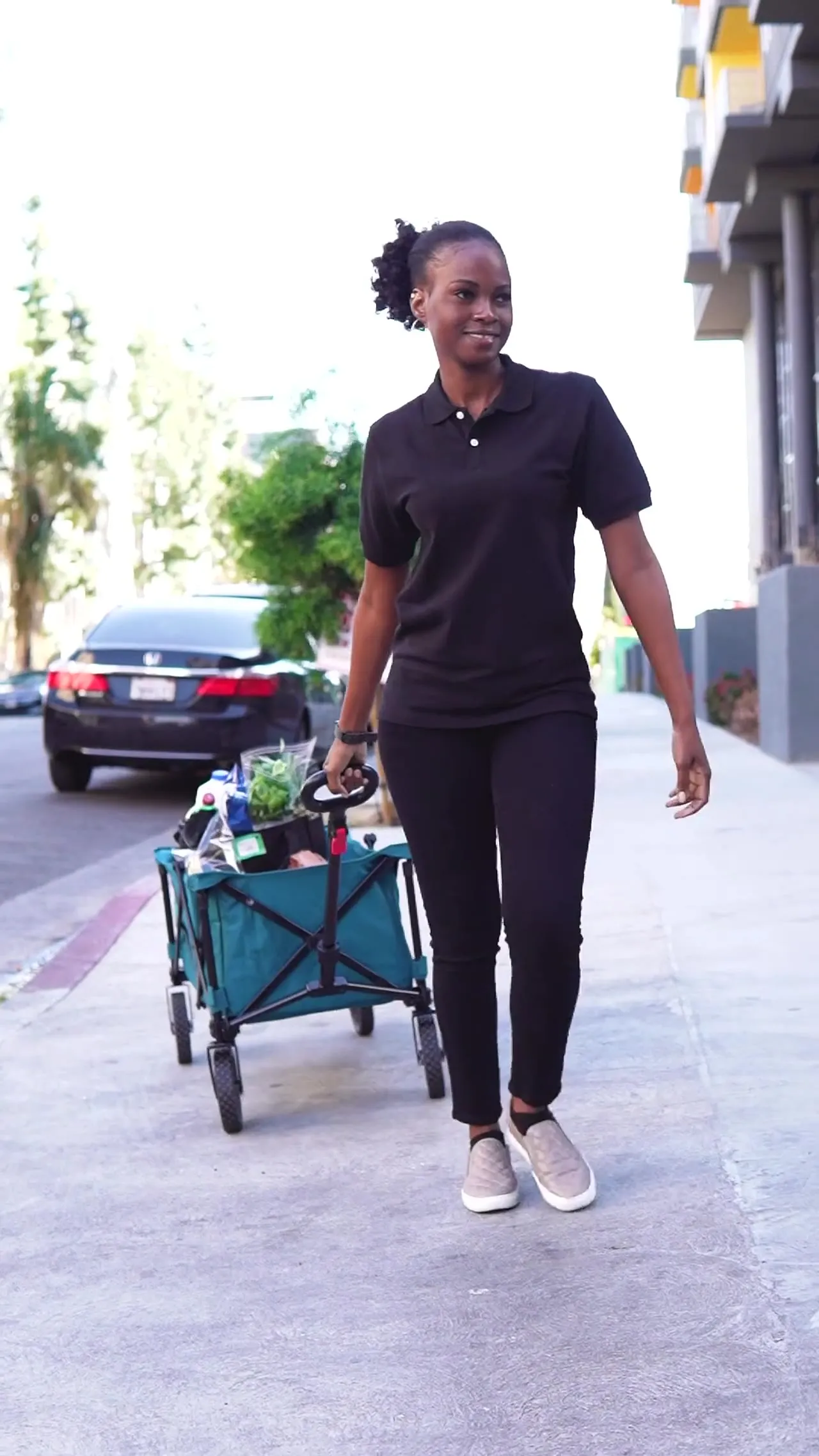 Smiling grocery shopper pulling a cart of groceries down a city sidewalk
